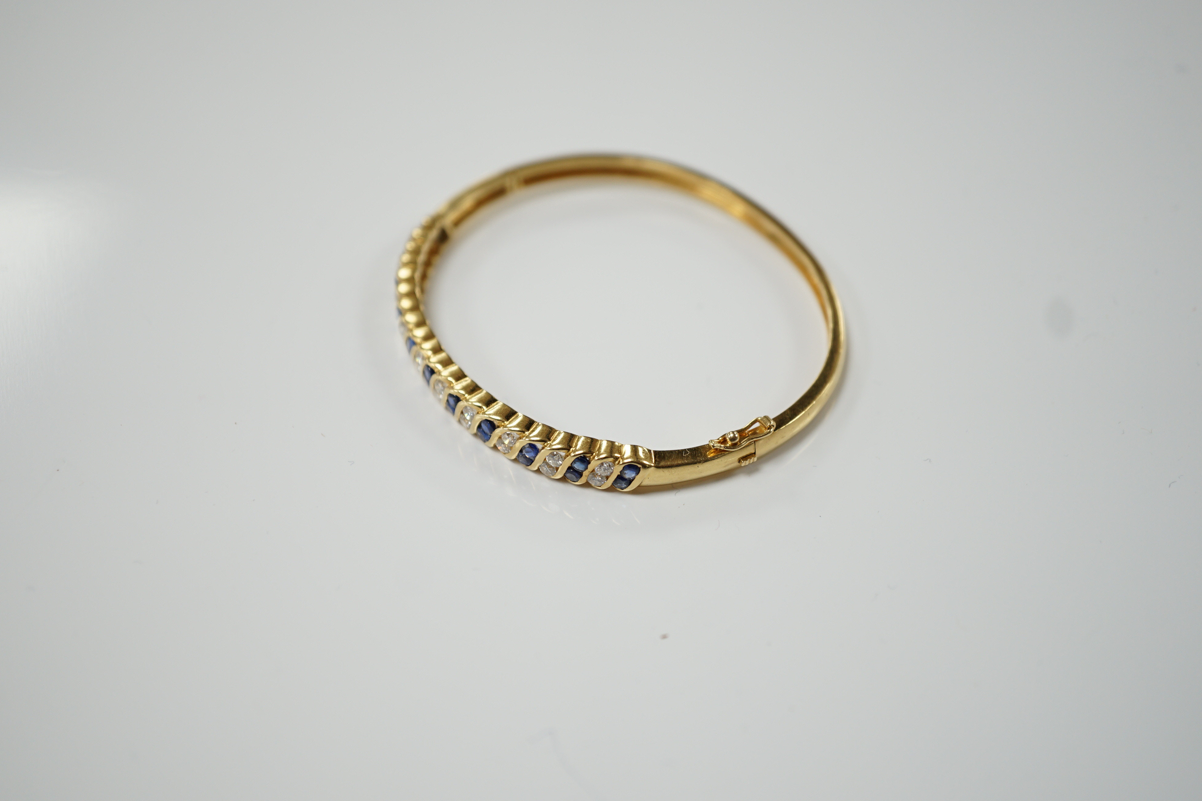 A 750 yellow metal, sapphire and diamond cluster set hinged bangle, interior diameter 56mm